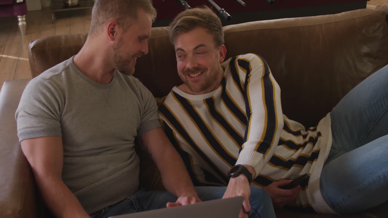 카우카시안 남성 커플이 집에서 소파에서 사회적 거리를 유지하고 있습니다.