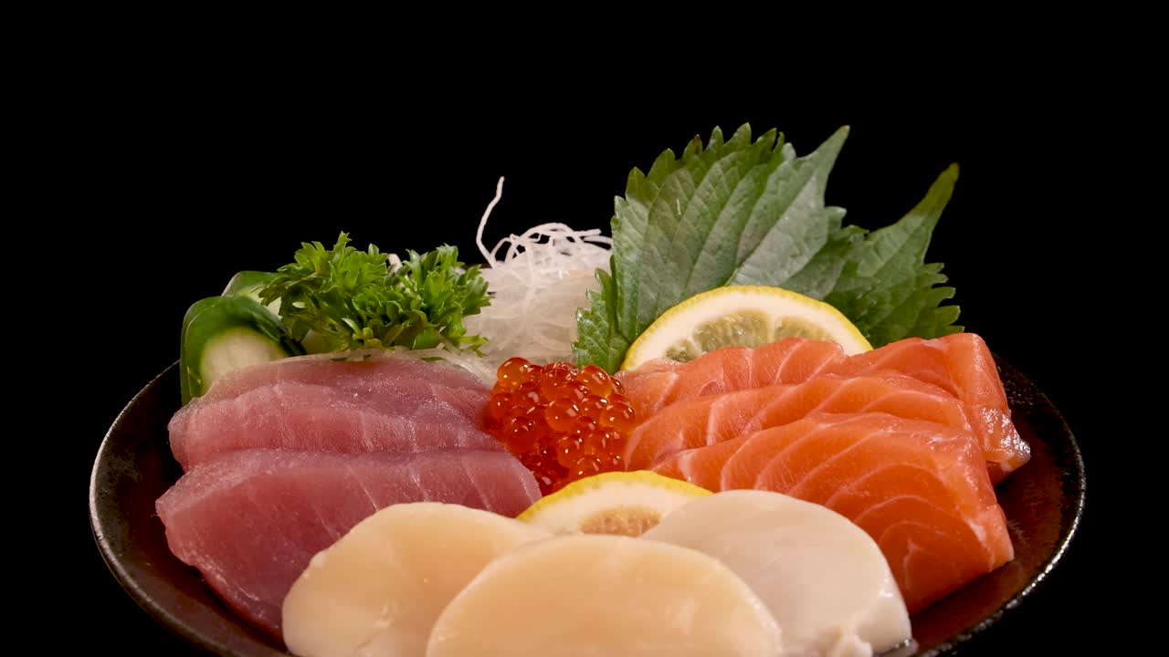 Assorted sashimi and sushi set with salmon, tuna, scallop, roe, and garnish, smoothly rotating on a seamless black background under studio lighting
