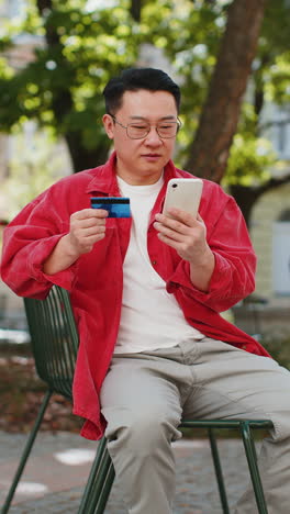 asian man using credit bank card smartphone while transferring money purchases online shopping