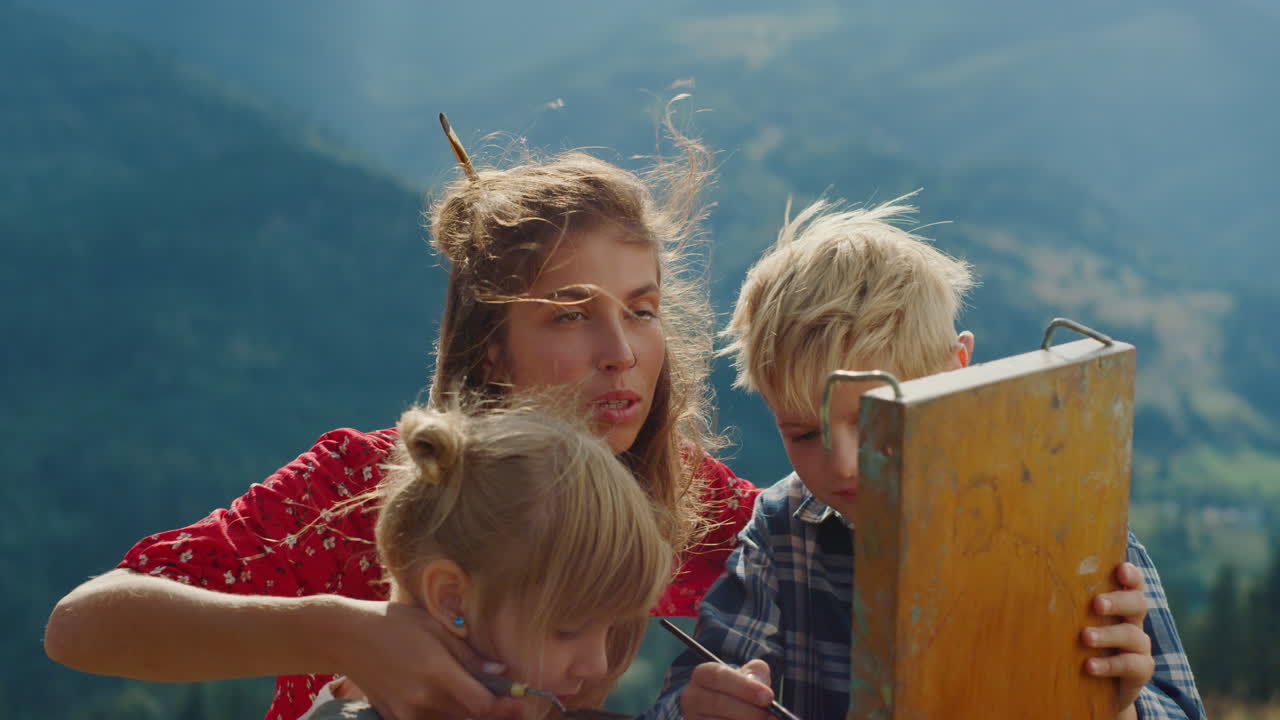 Lykkelig familie tegner fjell sammen. Nærbilde av mor med barn maler utendørs.