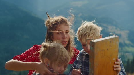 familia feliz dibujando montañas juntos. closeup madre con niños pintando al aire libre