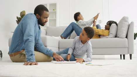 father with small son coloring picture with pencils on floor in living room