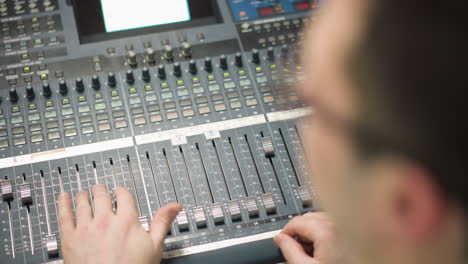 close-up of broadcast sound mixing desk. hands adjusting sound levels on faders, professional audio equipment in control room. audio operator focused on controlling live production sound