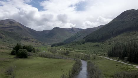 4k aerial drone footage zooming in above scottish highlands countryside with river and mountains