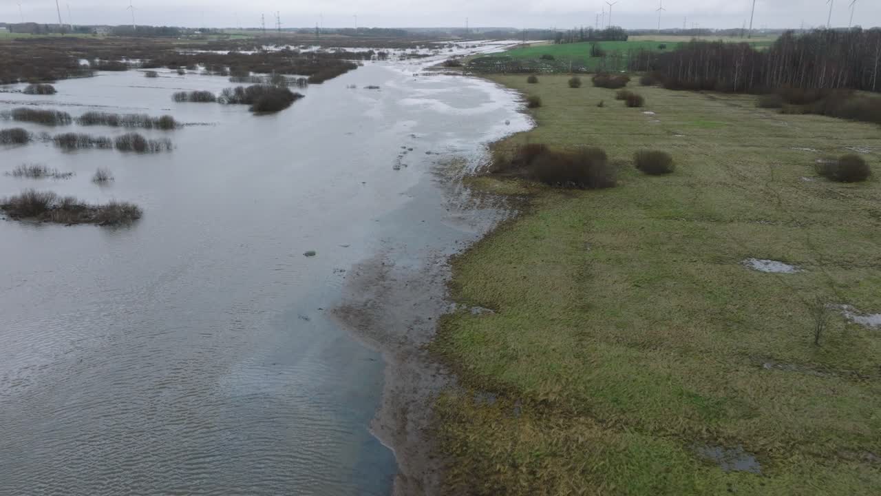 Aerial establishing view of high water in springtime, Alande river flood, brown and muddy water, agricultural fields under the water, overcast day, wide drone shot moving forward, tilt down