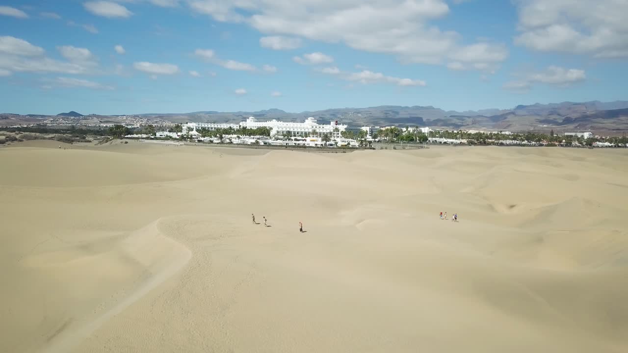 4K aerial footage of people walking in the Maspalomas desert with the stunning Hotel Rio Palace Maspalomas in the background.