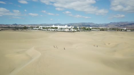 4k aerial footage of people walking in the maspalomas desert with the stunning hotel rio palace maspalomas in the background.