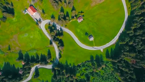 imágenes aéreas de drones de una carretera rural de un país en medio de campos verdes y árboles y casas cercanas durante el verano mientras el sol está brillando