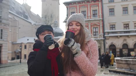 dos mujeres sonrientes turistas viajando juntos, bebiendo té caliente, café de tazas en la calle de la ciudad
