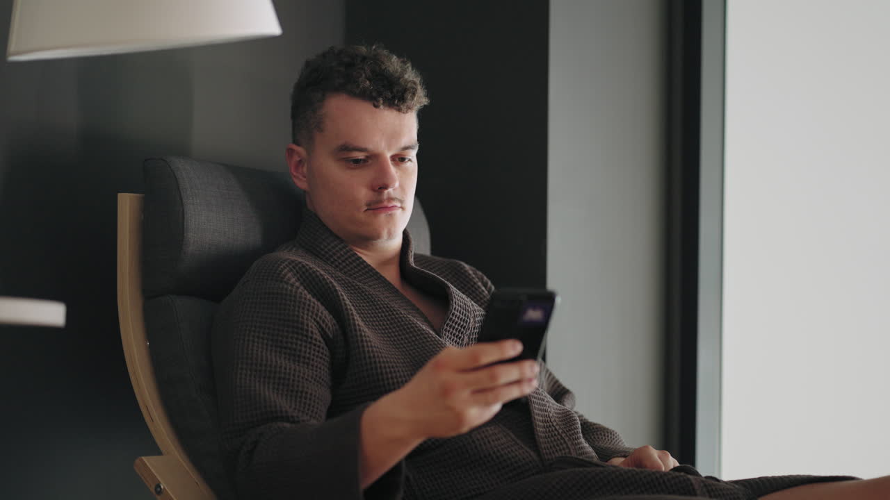 스파 살롱의 남성 방문자가 스마트폰을 사용하고 소셜 미디어를 보면서 치료 후 휴식을 취하고 있습니다.