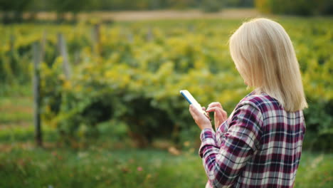 Eine-Bäuerin-Benutzt-Ein-Smartphone-Vor-Dem-Hintergrund-Seines-Kleinen-Weingutbesitzers