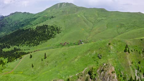 aerial view of green mountains and small village revealing from behind the hill