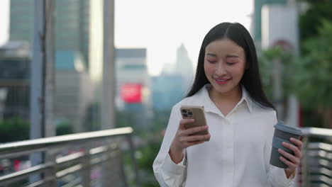 smiling asian woman using smartphone and holding coffee cup in city