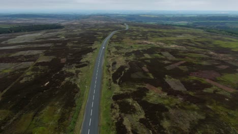 drone-view-of-long-winding-country-road-cutting-through-the-large-countryside-along-the-top-of-mountain-valley-on-cloudy-day-in-England-with-small-car-driving-in-the-distance