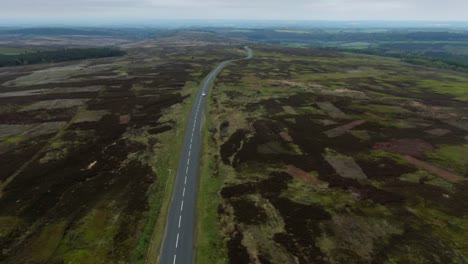 drone view of long winding country road cutting through the large countryside along the top of mountain valley on cloudy day in england with small car driving in the distance