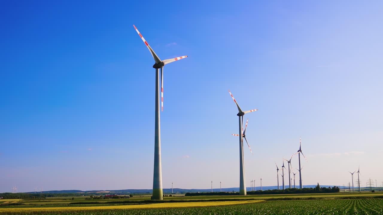 Wind turbines harness field energy. Several wind turbines stand tall against a clear blue sky in a rural area, showcasing renewable energy in action