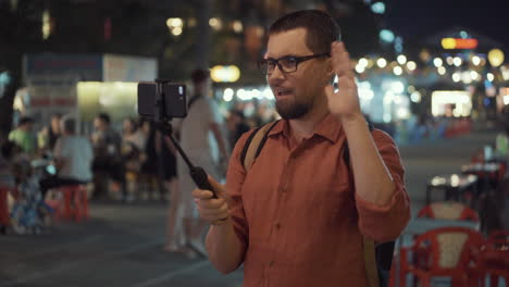 man taking a video with a selfie stick on a city night street