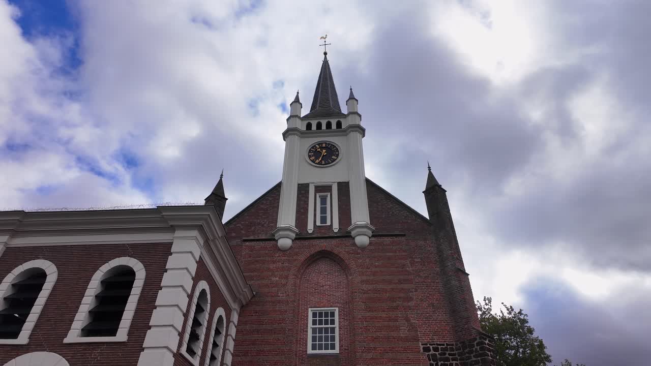 Close-up of Ommen church tower with white spire, black clock, and historic brickwork under a dramatic cloudy sky. Location: Ommen, Netherlands Ommen, Nederland