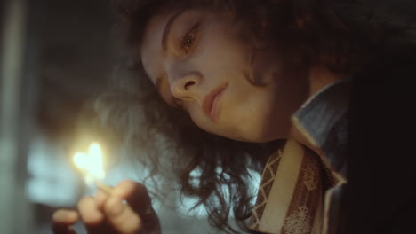 a young woman gazes at a lit matchstick in a dim setting