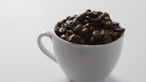 video de una taza de granos de café marrón tostados sobre un fondo blanco