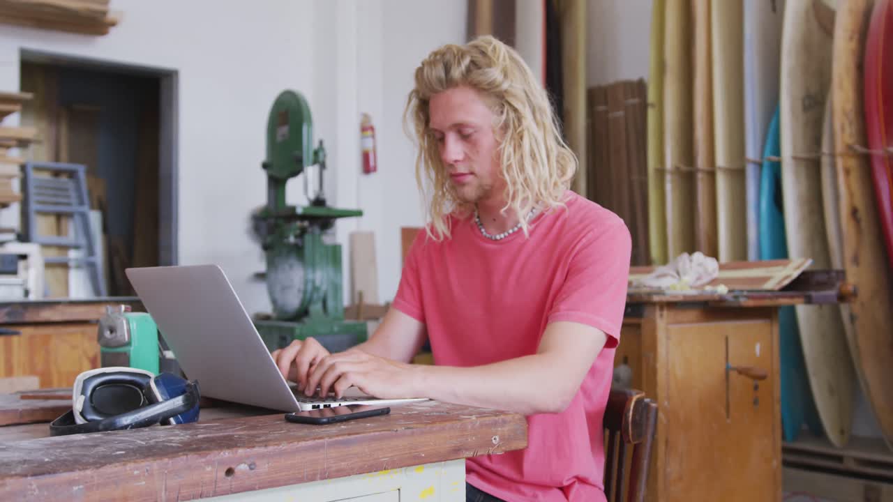 Un produttore di tavole da surf caucasico che lavora al suo laptop.