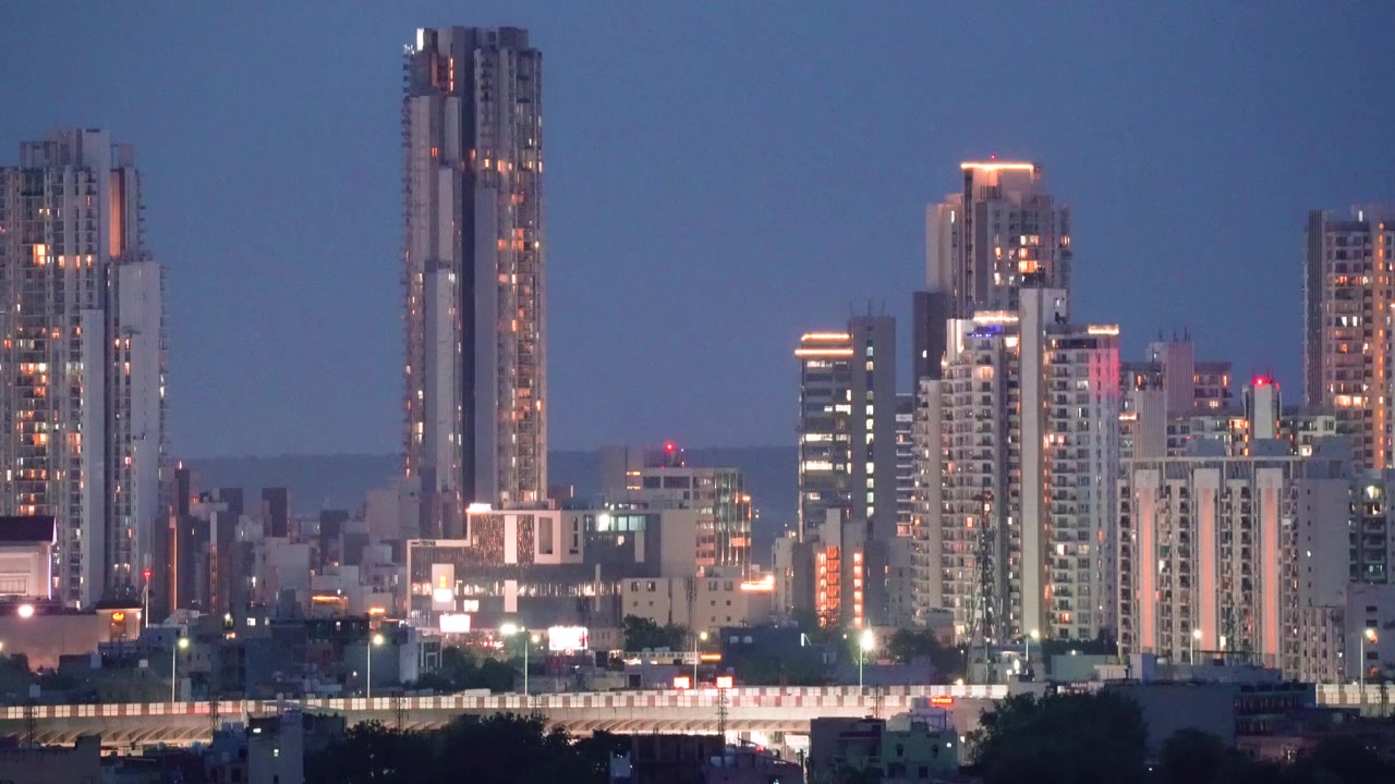 Tomada aérea de drone com zoom de arranha-céus altos e de vários andares com uma estrada elevada à frente, filmada ao entardecer, mostrando a paisagem urbana de Gurgaon, Delhi, Noida, Índia.