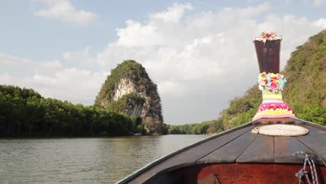 cámara lenta de un bote de cola larga tailandés de madera decorado con flores de colores flotando río abajo durante la puesta de sol con montañas de piedra caliza y bosques de manglares en la ciudad de krabi tailandia