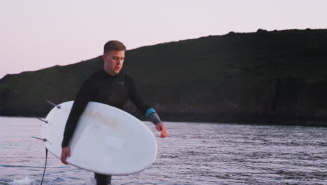 Mann-Im-Neoprenanzug-Mit-Surfbrett,-Als-Er-Aus-Dem-Meer-Geht