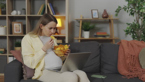 pregnant woman eating chips while working from home