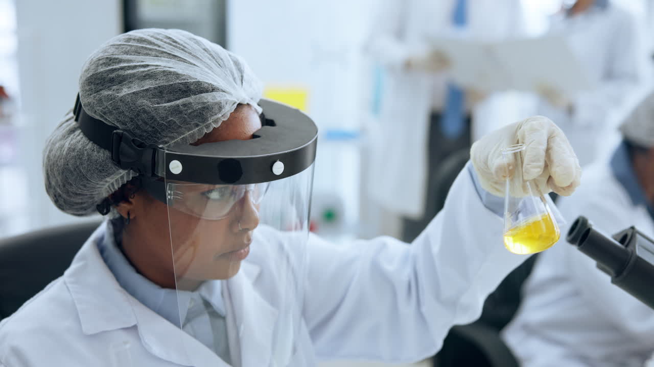 Focused Female Scientist Examining a Flask with Yellow Liquid in Lab