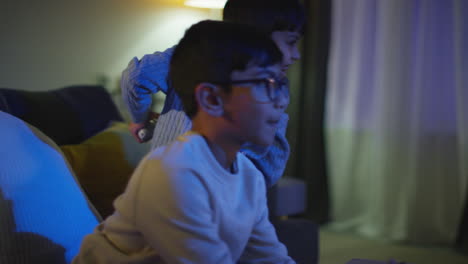 two young boys at home having fun playing with computer games console on tv fighting over controllers late at night 1