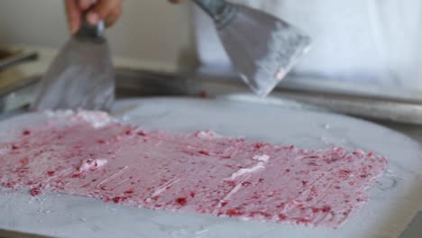 rolled ice cream dessert with chopped strawberries prepared with a spatula over a freezing-cold stainless steel surface