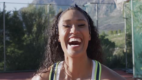 Portrait-of-happy-biracial-female-basketball-player-on-sunny-court,-in-slow-motion