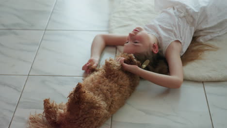 little girl lying on floor playing with pet dog, cuddling and having fun with furry companion, spending quality time together at home on cozy blanket