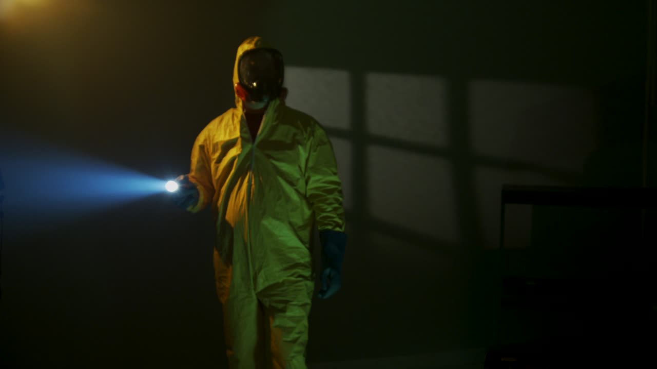 Hazmat suit wearing man explores a dark room