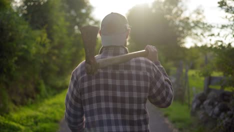 Lumberjack-walking-in-the-countryside-at-sunset,-with-an-axe-on-his-shoulder,-with-beautiful-flares