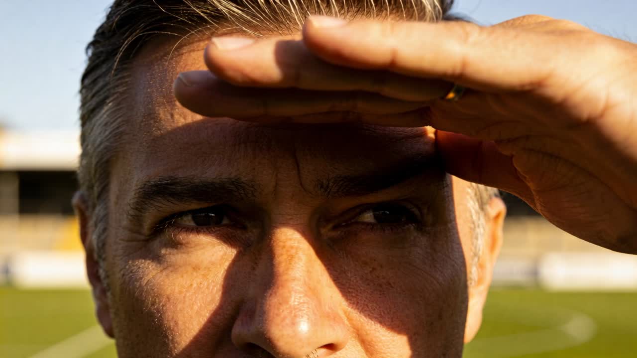 Uomo che si ripara la fronte con la mano destra, mostrando un anello, su un campo sportivo, concentrandosi sul gioco.
