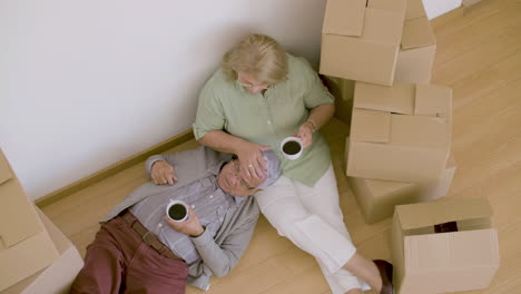 tired senior couple lying on floor and drinking tea after moving