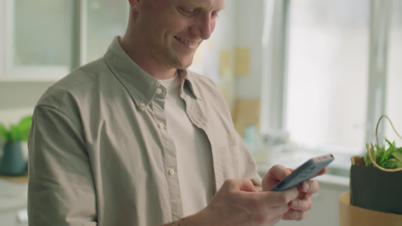 Man Using Phone and Smiling in Kitchen at Home