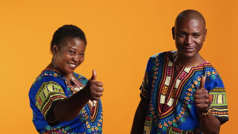 Joyful-husband-and-wife-doing-thumbs-up-sign-in-studio