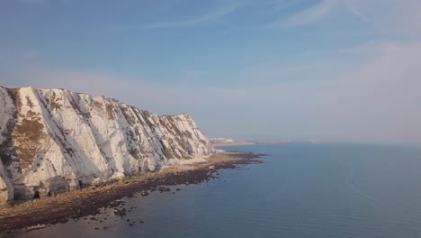 drone flies low away from the white cliffs of dover with beautiful turquoise sea in the foreground