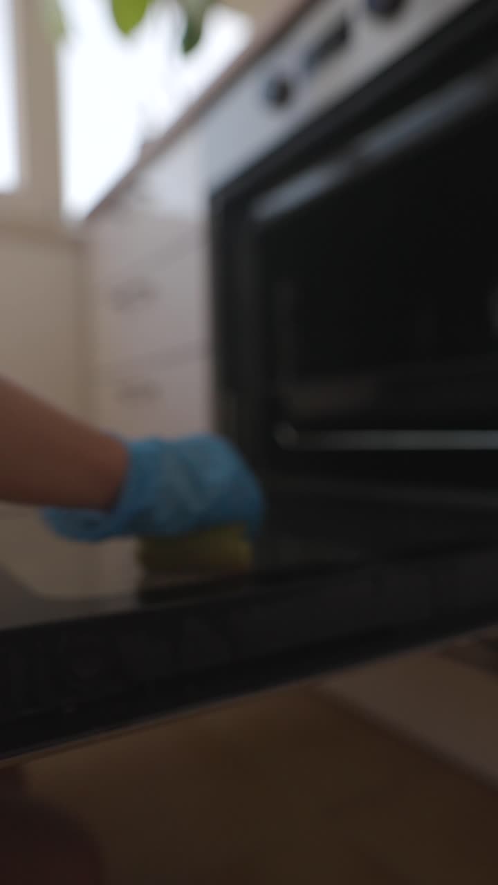 Donna che pulisce lo sportello del forno con una spugna in cucina