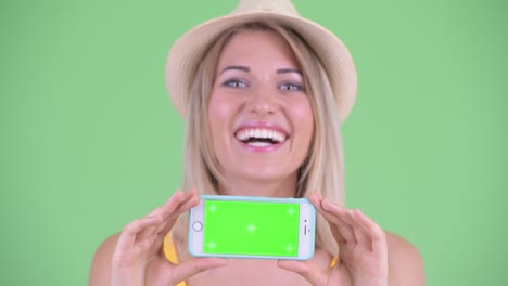 fotografía de estudio de una joven turista sonriendo y mostrando un teléfono móvil con clave de croma copia el espacio contra un fondo verde