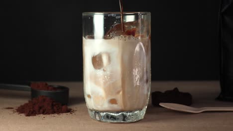 iced coffee being poured into a glass with milk and ice cubes, coffee grounds in frame