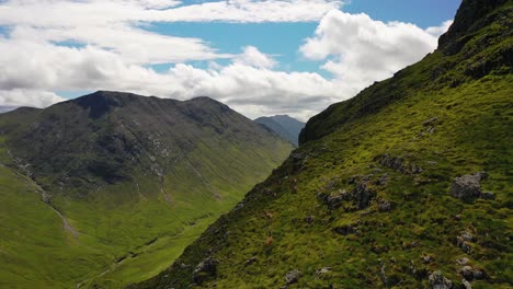 Scottish-Highlands-Aerial-of-a-Herd-of-Red-Deer-walking-along-Cliffs-in-a-Scottish-Valley-in-Glencoe-Mountains,-Scotland,-United-Kingdom