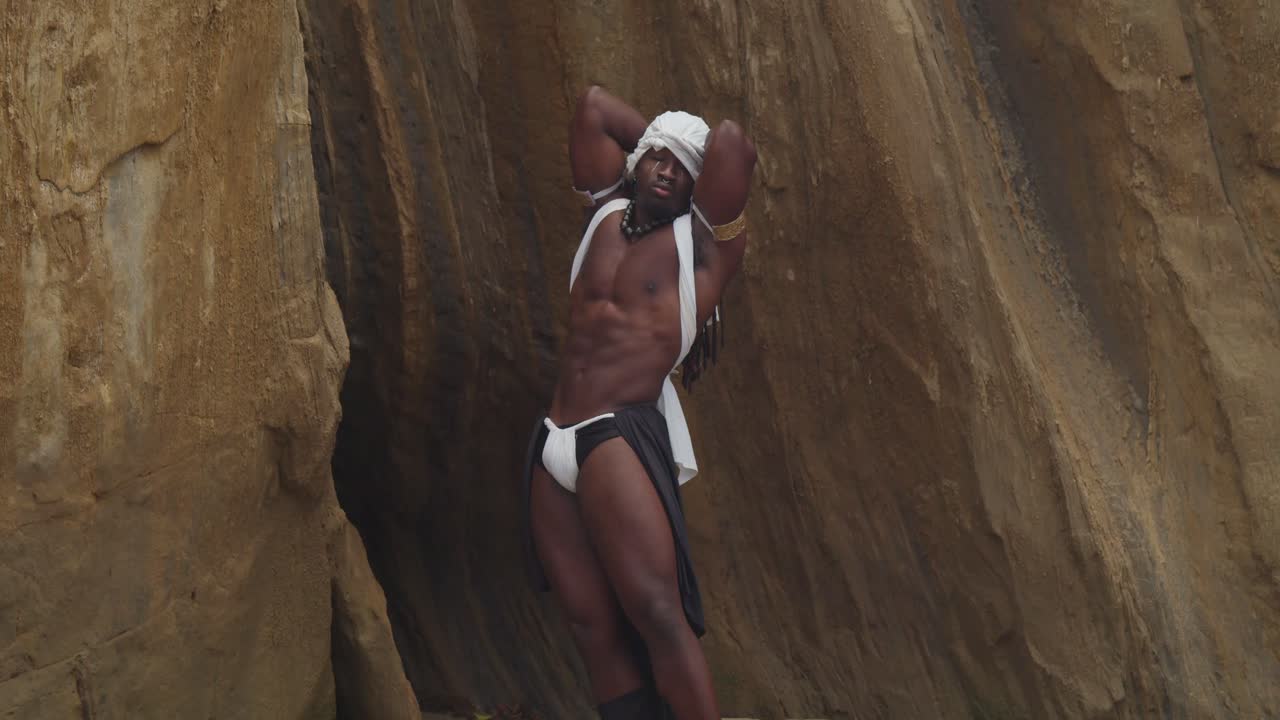 On the sandy shore, a muscular male cosplayer with dark skin.