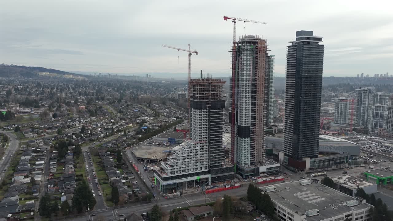 Construcción de rascacielos con grúas en un barrio residencial bajo un cielo nublado. Burnaby, BC, Canadá. Toma de dron de alejamiento.