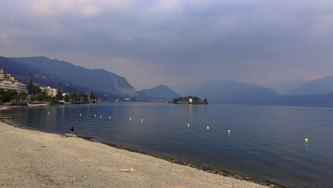 lakeshore of lake maggiore with hotels and alps mountain range in background on cloudy day, stresa in italy