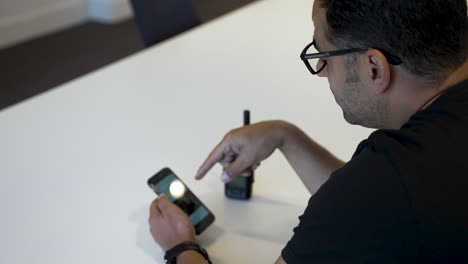 Ein-Europäischer-Mann-Mit-Brille,-Der-In-Einem-Konferenzraum-Sitzt-Und-Ein-Smartphone-Und-Ein-Walkie-Talkie-Benutzt