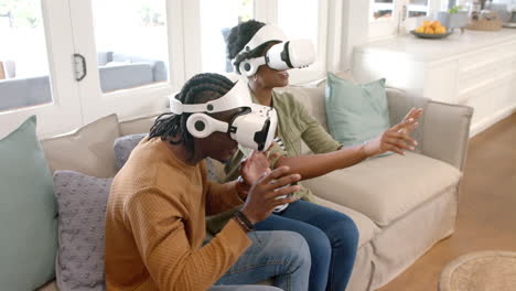Using VR headsets, African american couple sitting on couch and interacting with virtual world